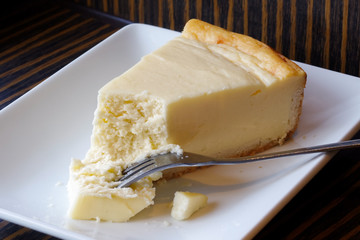 Plain baked cheesecake with cake on fork on white ceramic plate. Brown background.