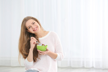 Young beautiful woman eating fresh salad on light background