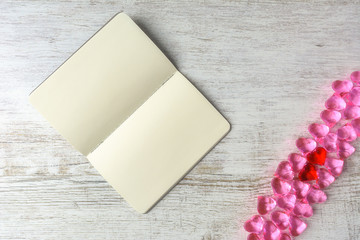 notebook on a wooden table, next to a pink glass hearts and two red in the middle
