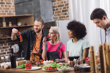 multiethnic friends tasting some food while cooking in kitchen