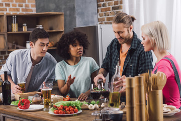 man pouring alcohol to multiethnic friends glasses