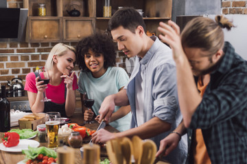 multiethnic girls drinking wine and looking at men cooking  in kitchen