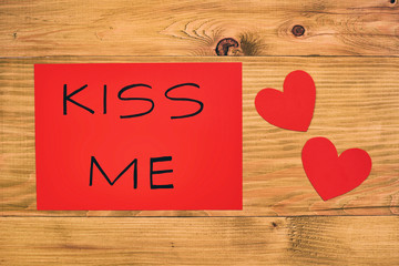 Red paper with message kiss me and heart shapes on wooden table.