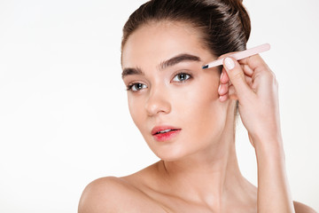 Naklejka premium Close up studio portrait of young brunette woman with soft skin plucking eyebrows with tweezers isolated over white background