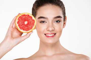 Joyful image of smiling half-naked woman with natural makeup holding orange citrus near her face and looking on camera over white background