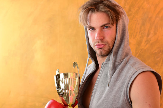 Guy in grey sleeveless hoodie holds golden prize