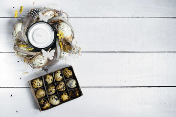 Easter spring decorative composition, crafted wreath with candle inside and box with quail eggs. Close up portrait on white wooden background with place for text.
