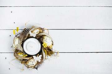 Easter spring decorative composition, crafted wreath with candle inside. Close up portrait on white wooden background with place for text.