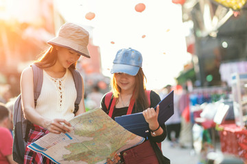 Beautiful woman traveler holding location map in hands while looking for some direction in street food china town.