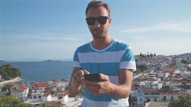 Smiley man using cellphone with small ocean town panorama in background