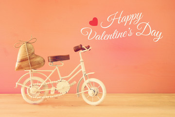 Valentine's day romantic background with white vintage bicycle toy and heart on it over wooden table.