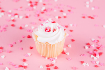 cup cake with white icing and heart sprinkles on a pink background for valentine's day