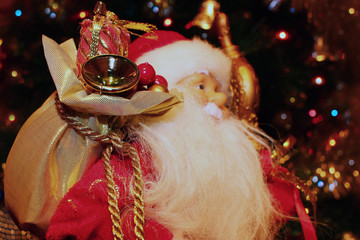 cheerful Santa Claus with a bag of presents against the festive lights of a Christmas tree.