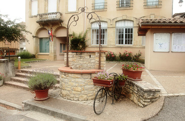 Fototapeta na wymiar Picturesque village square, featuring a well, old bicycle and flower pots, village in the South of France