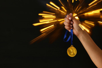 Woman hand holding gold medal against black background with glitter overlay. Award and victory concept.