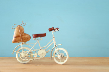 Valentine's day romantic background with white vintage bicycle toy and heart on it over wooden table.