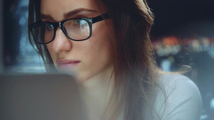 Beautiful young businesswoman wearing glasses and working at night using modern computer touchscreen, confident female employer working at new office with panoramic view of night city - Powered by Adobe