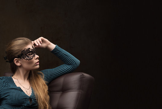 Young woman in black lace mask on the eyes looking to the side sitting on the couch