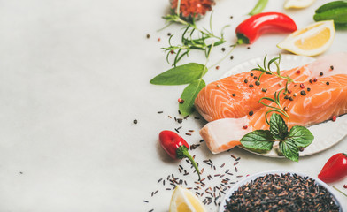 Raw salmon fish fillet steaks with vegetables, greens, rice, spices and lemon over light grey marble background, copy space. Clean eating, alkaline diet, dieting, power boosting, weight loss concept