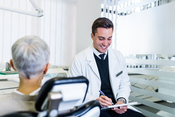 Handsome and attractive male dentist looking at dental x-ray together with his beautiful senior woman patient.