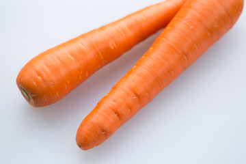 Pair long fresh raw carrot on a plastic cutting board is white color.