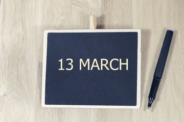 sentence MAR 13 written with chalkboard on a wooden table with pen.