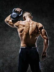 Fototapeta na wymiar Muscular back of man. Rear view of fitness model with kettlebell on dark background. Strength and motivation