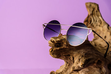 Fashionable sunglasses with purple lenses placed on timber. in purple background