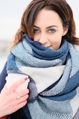 Portrait of attractive young woman wearing scarf and holding white coffee cup on a cold and snowy winter day