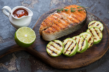 Rustic wooden serving board with grilled salmon fillet, zucchini slices and sauce, studio shot, selective focus