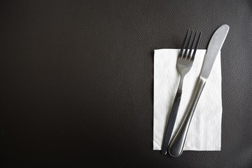 Set of fork and knives with tissue paper on dark brown leather in restaurant.