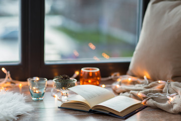 book, garland lights and candles on window sill