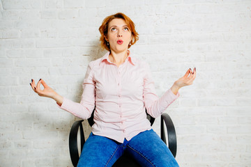 Portrait of red hair woman relaxing on the office chair indoors over white brick wall background.