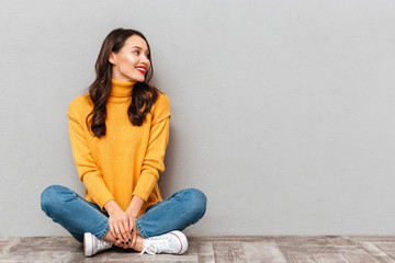 Happy brunette woman in sweater sitting on the floor