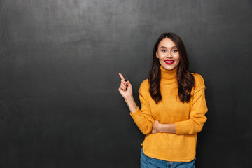 Smiling brunette woman in sweater pointing at copyspace