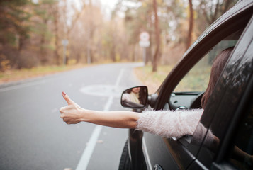 Female traveler on the road holding thumbs up. Fall vacation, holidays, travel, road trip and...