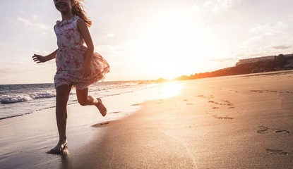 Happy little girl running on the beach at sunset