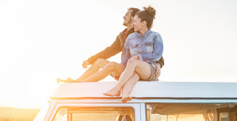 Happy couple sitting on top of minivan roof at sunset