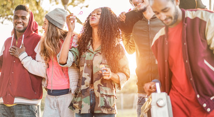 Group of happy friends walking and listening music in city park