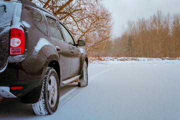 Naklejka premium Dark car on a snowy road on a winter trip close-up of a tire protector, concept of danger on the roads in weather conditions while traveling