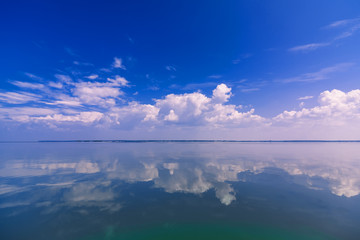 blue clear sky with white clouds reflected in calm water of sea on Sunny day