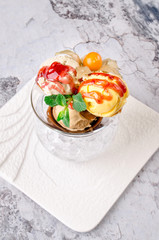 Top view close up. Three balls of multi flavor ice cream with Scoops of Chocolate, Vanilla and Fruit Ice Cream with Fresh Mint in Glass Dish on a white plate on a gray background.