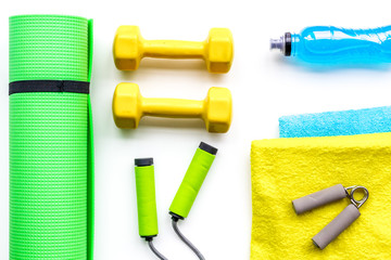 Do fintess in gym. Dumbbells, jump rope, expander, mat, water on white background top view pattern