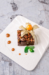 Top view piece of delicious chocolate brownie with nuts and green mint on white plate on gray background. Restaurant kitchen.