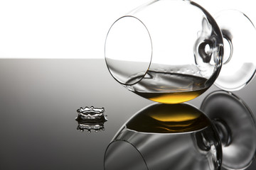 Brandy in a cognac glass lying on its side on shiny surface with drop splash
