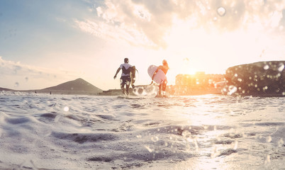 Surfers couple running with surf boards on the beach - Sporty people having fun in sunny day - Extreme sport, travel and vacation concept - Focus on bodies - Water on camera lens