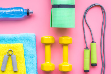 Fitness background. Equipment for gym and home. Jump rope, dumbbells, expander, mat, water on pastel pink background top view