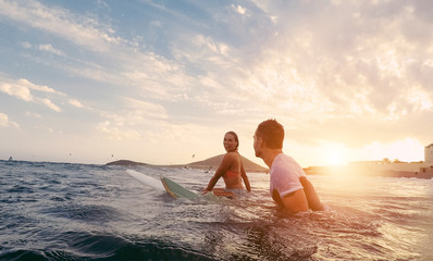 Fit couple surfing at sunset - obrazy, fototapety, plakaty