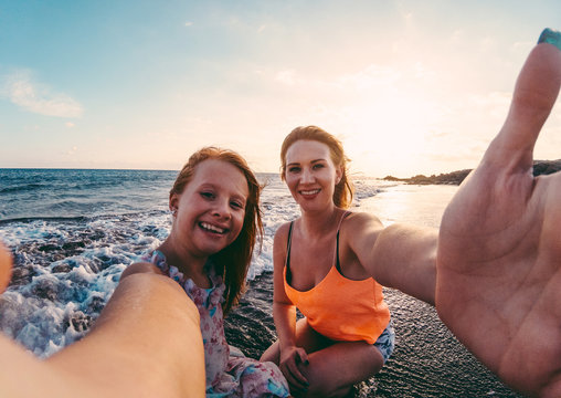 Red hair mother and daughter taking selfie photo with smartphone camera on the beach