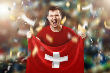 Fototapeta premium A Swiss fan, a fan of a man holding the national flag of Switzerland in his hands. Soccer fan in the stadium. Mixed media